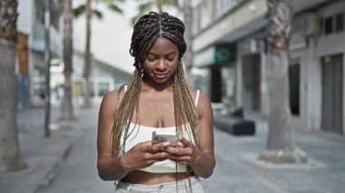 Sokakta gülümseyen akıllı telefon kullanan Afrikalı Amerikalı kadın.