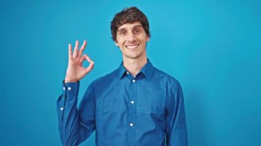 Genç İspanyol adam mavi arka planda gülümsüyor.