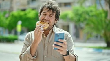 Sokakta akıllı telefon kullanan İspanyol bir adam donut yiyor.