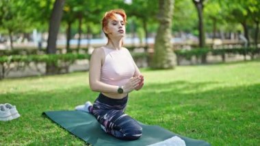 Genç kızıl saçlı kadın yoga egzersizi yapıyor parkta otun üzerinde oturuyor.