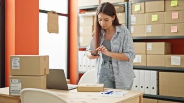 Genç ve güzel İspanyol kadın ecommerce işçisi ofiste fotoğraf paket yapıyor.