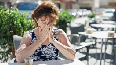 Orta yaşlı bir kadın kahve dükkanının terasında oturmuş akıllı telefon kullanıyor.