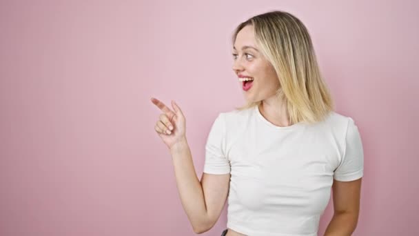 Молода Блондинка Посміхається Вказуючи Бік Пальцем Здивованим Над Ізольованим Рожевим — стокове відео