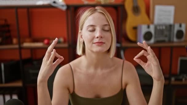 ポッドキャストスタジオでヨガの練習をしているテーブルに座っている若い金髪の女性ミュージシャン — ストック動画
