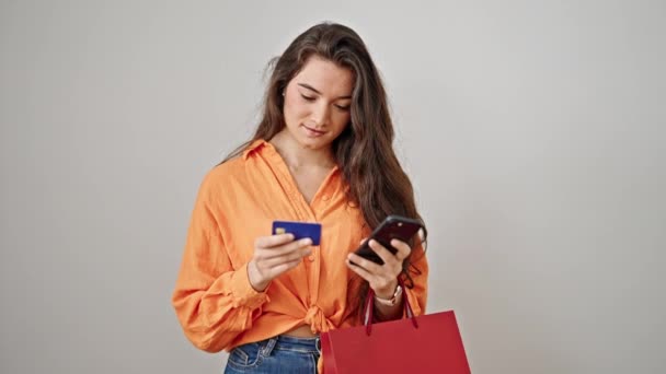 若い美しいヒスパニック系の女性が隔離された白い背景の上にスマートフォンやクレジットカードを使用してショッピングバッグを保持 — ストック動画