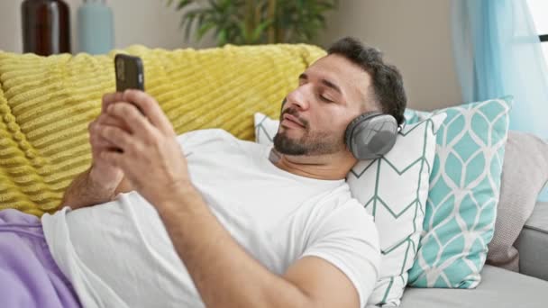 Jovem Árabe Homem Usando Smartphone Fones Ouvido Deitado Sofá Casa — Vídeo de Stock