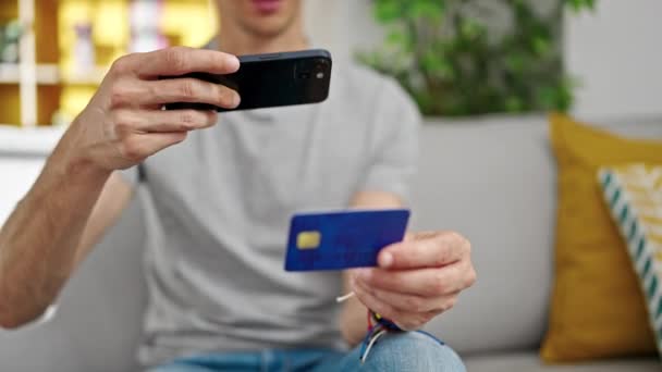 若いヒスパニックの男は自宅でスマートフォンでクレジットカードに写真を作ります — ストック動画