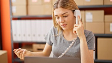 Genç sarışın kadın ecommerce iş işçisi telefonda konuşuyor.