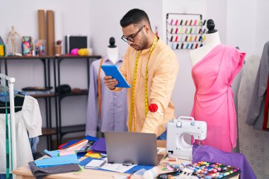 Genç İspanyol terzi terzide dokunmatik ped ve dizüstü bilgisayar kullanıyor.