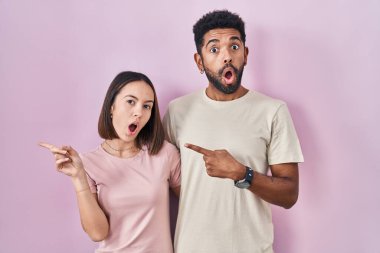 Pembe arka planda genç İspanyol çift parmaklarını yana doğru göstererek şaşırdı, ağzı açık hayret içinde kaldı.. 
