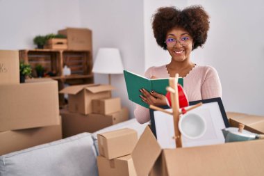 Afro-Amerikalı bir kadın gülümseyerek evde kendinden emin bir şekilde kitap okuyor.