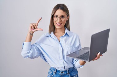 Bilgisayarda çalışan genç bir kadın gülümseyen ve el hareketleriyle hareket eden parmaklarıyla işaret eden ve kamerasını gören bir bilgisayarla çalışıyor. ölçüm kavramı. 