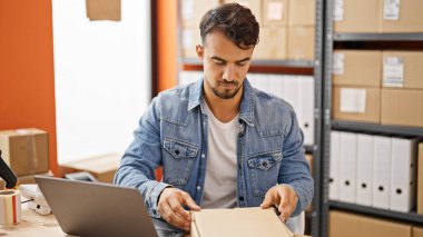 Young hispanic man ecommerce business worker packing cardboard box at office