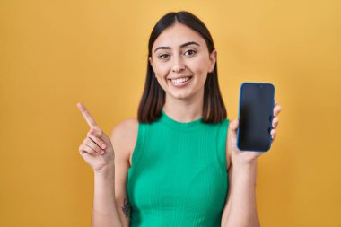 Akıllı telefon tutan İspanyol kız ekranda gülümsüyor. Elleri ve parmakları kenarda mutlu bir şekilde gösteriyor. 