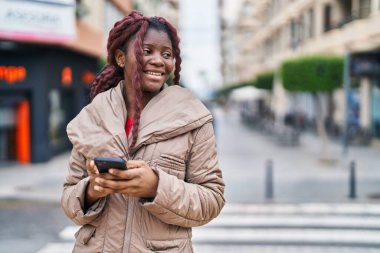 Afro-Amerikalı kadın sokakta akıllı telefon kullanarak kendine güveniyor.