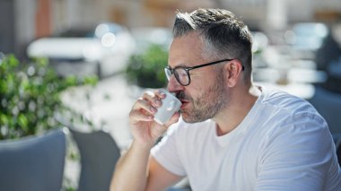 Kahve içen gri saçlı adam kahve dükkanının terasında oturuyor.