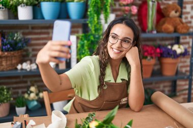 Genç ve güzel İspanyol çiçekçi çiçekçi çiçekçide akıllı telefondan selfie çekiyor.