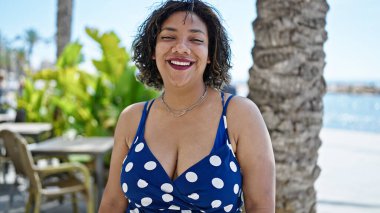 Kahve dükkanının terasında kendine güvenen güzel Latin kadın gülümsüyor.