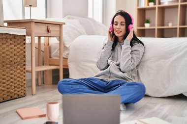 Beyaz kız öğrenci müzik dinliyor. Yatak odasında yerde ders çalışıyor.