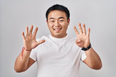 Beyaz arka planda duran genç Çinli adam dokuz numarayı gösterip işaret ederken kendinden emin ve mutlu gülümsüyor.. 