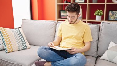 Evdeki kanepede oturmuş kitap okuyan genç bir İspanyol.