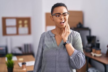 Ofiste çalışan Afrika kökenli Amerikalı bir kadın diş ağrısı ya da diş hastalığından dolayı elleriyle dudaklarına dokunan gözlüklerle acı dolu bir ifade takınıyor. dişçi 