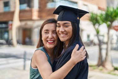 Two women mother and graduated daughter hugging each other at street