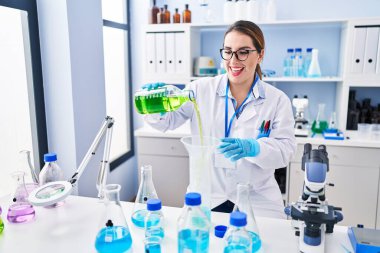 Genç ve güzel İspanyol bilim kadını laboratuarda test tüpüne sıvı döküyor.