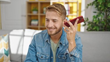Kafkasyalı genç adam evdeki kanepede oturan akıllı telefondan sesli mesajı dinliyor.