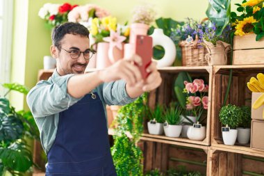 Young hispanic man florist make selfie by smartphone at flower shop