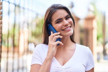 Gülümseyen genç bir kadın caddedeki akıllı telefondan konuşuyor.