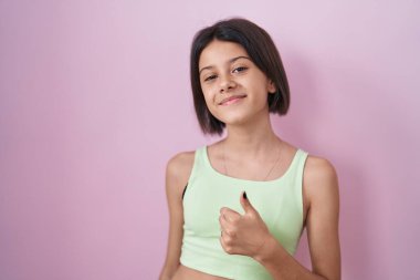 Pembe arka planda duran genç kız elleriyle mutlu bir jest yapıyor. Kameraya bakıp başarıyı gösteren ifade. 