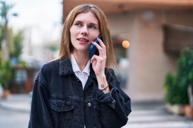 Genç sarışın kadın gülümsüyor. Kendine güveni tam. Akıllı telefondan konuşuyor.