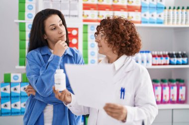 Eczanede ilaç yazan iki kadın eczacı ve müşteri var.