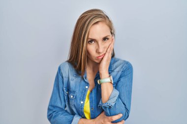 Mavi arka planda duran genç sarışın kadın çapraz kollu depresyondan sıkılmış ve yorgun görünüyor.. 