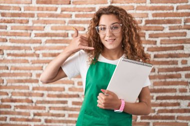 Genç beyaz bir kadın sanat defteri tutuyor gülümsüyor telefonla el ve parmak hareketleri yapıyor telefonda konuşuyor gibi. iletişim kavramları. 