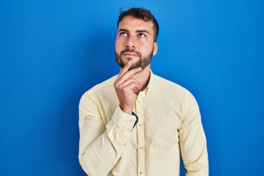 Mavi arka planda duran yakışıklı İspanyol adam şüphe üzerine yoğunlaşmıştı. Parmakları çenesinde ve yukarı bakıyordu. 