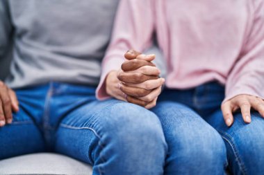 Man and woman couple sitting on sofa with hands together at home