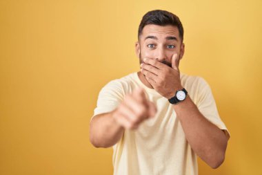 Sarı arka planda duran yakışıklı İspanyol adam sana gülüyor, eli ağzında kamerayı işaret ediyor, yüz ifadesi utanç verici. 