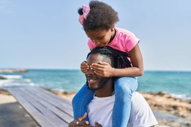 Father and daughter smiling confident holding girl on shoulders at seaside