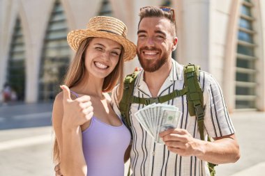 Ellerinde dolar tutan genç turist çifti mutlu ve olumlu gülümsüyor, başparmakları mükemmel ve onay işareti yapıyor. 