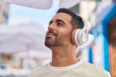 Sokakta müzik dinlerken kendinden emin gülümseyen İspanyol genç adam.