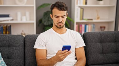 Evdeki kanepede oturan, akıllı telefon kullanan genç bir İspanyol.