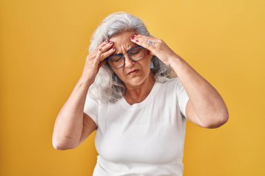Sarı arka planda gri saçlı, başı ağrıyan orta yaşlı bir kadın. Stres yüzünden. migren ağrısı. 