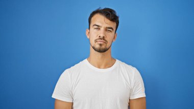 Soyutlanmış mavi arka planda ciddi bir ifadeyle duran İspanyol genç adam.