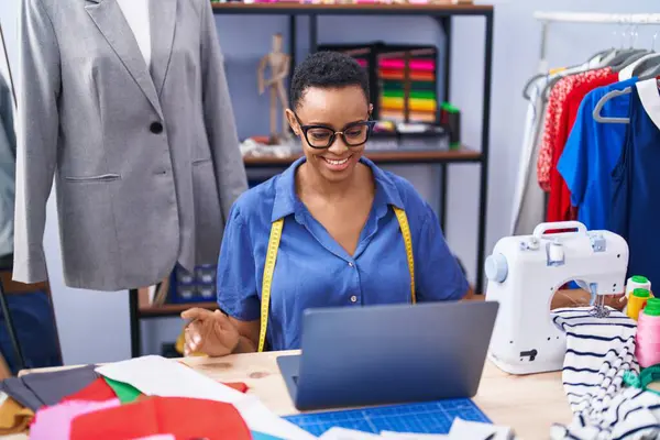 African american woman tailor smiling confident using laptop at tailor shop