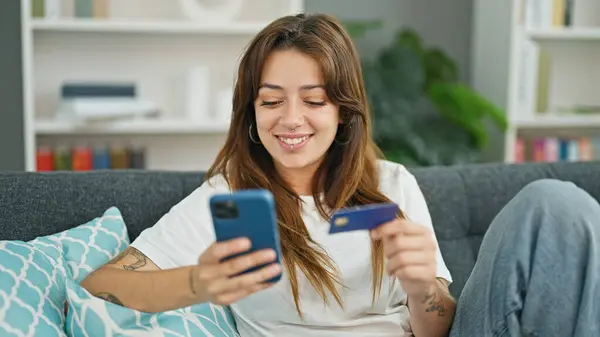 年轻美丽的惊慌失措的女人带着智能手机和信用卡在家里沙发上购物 — 图库照片