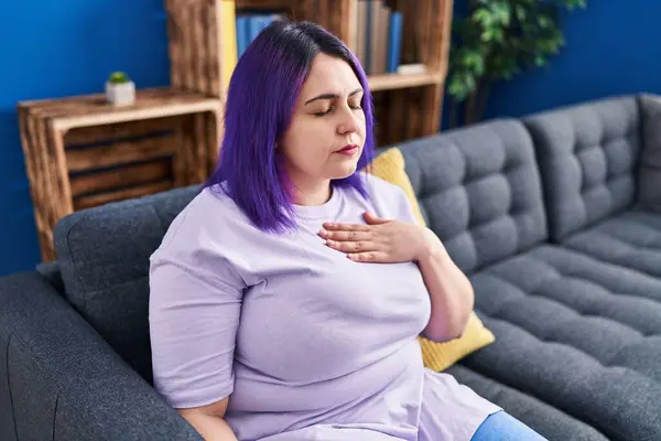 Young beautiful plus size woman sitting on sofa suffering anxiety attack at home