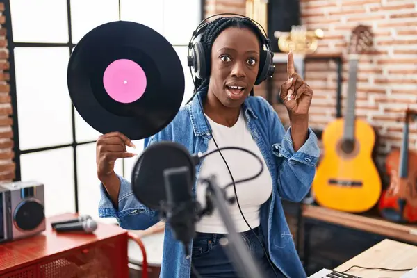 Beautiful black woman holding vinyl record at music studio smiling with an idea or question pointing finger with happy face, number one