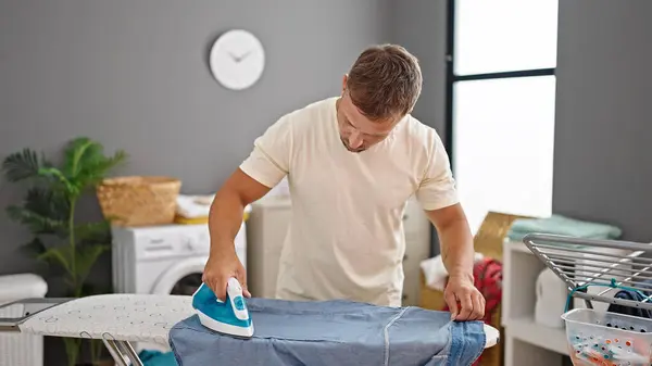 Young man ironing clothes at laundry room